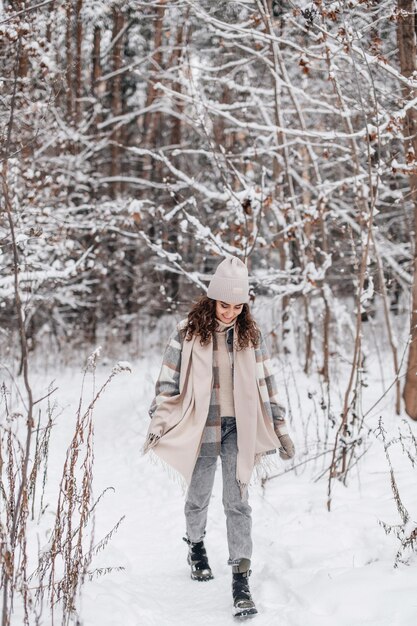 Photo une jolie fille dans un manteau et un chapeau se promène dans une forêt enneigée le long d'un sentier