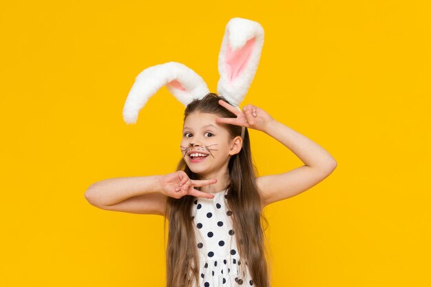 Jolie fille dans les oreilles de lapin de Pâques fantaisie et moustache peinte sur un fond isolé jaune Vacances de printemps de Pâques Une fille dans les oreilles d'un lapin de Pâques