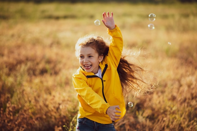 Une jolie fille dans un parc jaune joue et s'amuse avec des bulles de savon au coucher du soleil. Enfance.