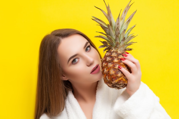Jolie fille dans un peignoir tenant un ananas sur un jaune