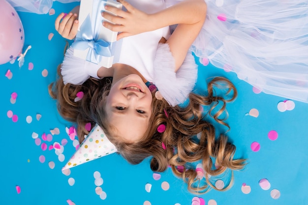 Jolie fille dans une robe blanche moelleuse avec un cadeau dans ses mains se trouve sur un fond bleu en confettis