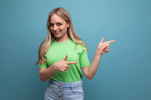 Jolie fille dans une tenue décontractée pointe vers un espace vide sur fond bleu