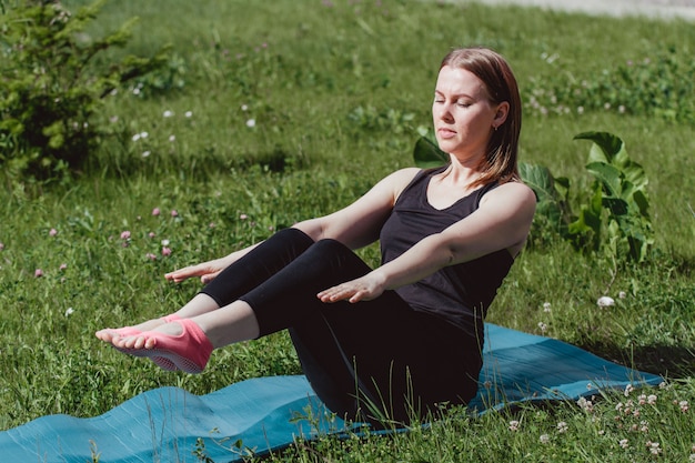 Jolie fille dans des vêtements noirs sur l'herbe verte, faire du yoga. Style de vie sportif