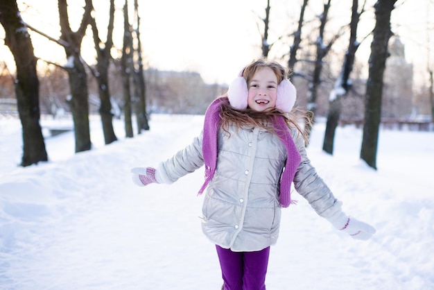 Jolie fille drôle d'enfant marche dans un parc enneigé sur fond de nature à l'extérieur