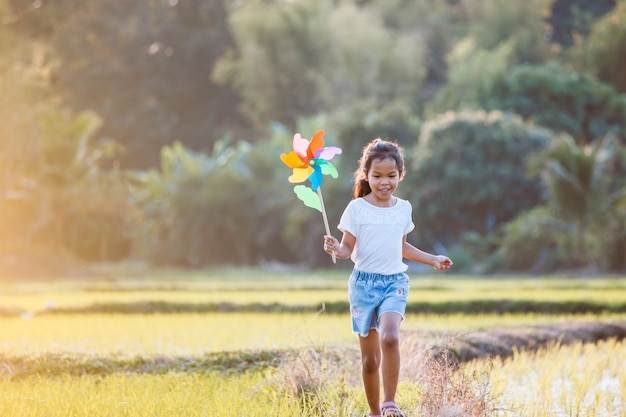 Jolie fille enfant asiatique est en cours d'exécution et joue avec un jouet d'éolienne avec plaisir dans la rizière