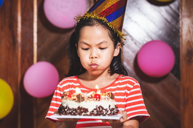 Jolie fille enfant asiatique souffle des bougies sur un délicieux gâteau d'anniversaire dans la fête avec plaisir et bonheur