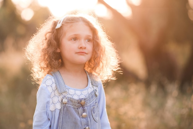 Jolie fille d'enfant posant dans medow dans la lumière du soleil à l'extérieur