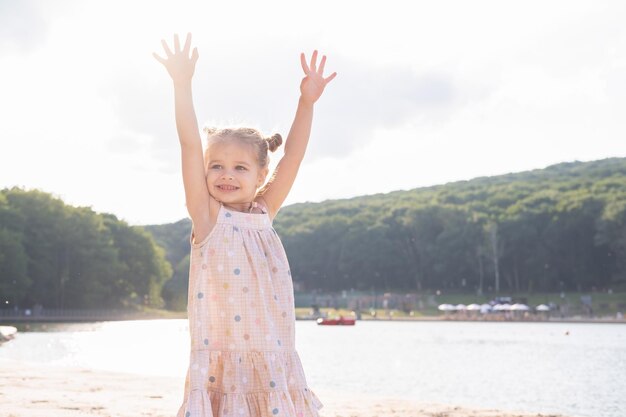 Jolie fille enfant en robe avec des queues drôles mains en l'air s'amusant sur la nature le jour d'été ensoleillé