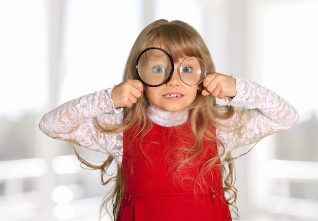 Photo jolie fille enfant s'amuser avec des loupes sur fond de chambre floue