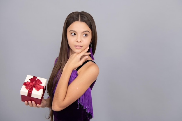 Jolie fille enfant tenir boîte de cadeau d'anniversaire enveloppée de ruban rouge arc fond gris copie espace shopping