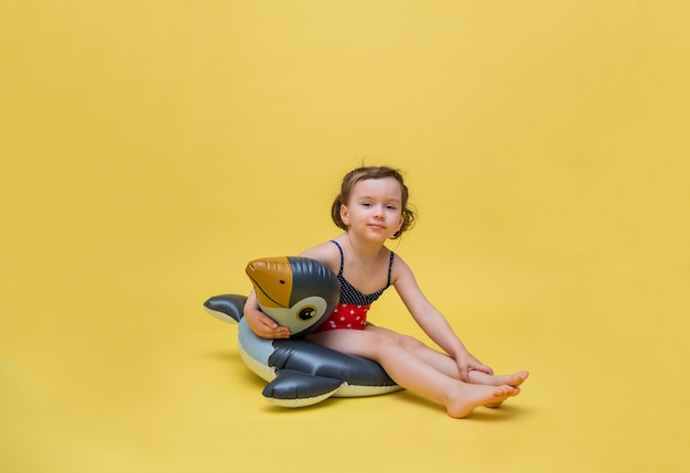 Une jolie fille est assise dans un cercle de natation sur un espace jaune. Une petite fille en maillot de bain à pois ressemble. Un cercle pour nager en forme de pingouin