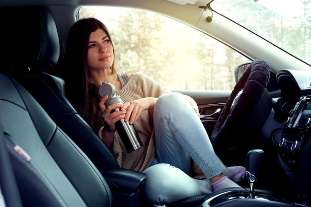 Jolie fille est assise dans une voiture et boit du café voyage d'hiver
