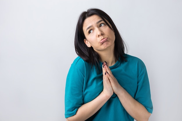 Jolie fille à l'expression impuissante, demande de l'aide, maintient les paumes pressées l'une contre l'autre.