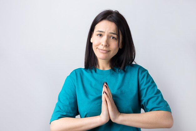 Jolie fille à l'expression impuissante, demande de l'aide, maintient les paumes pressées l'une contre l'autre.