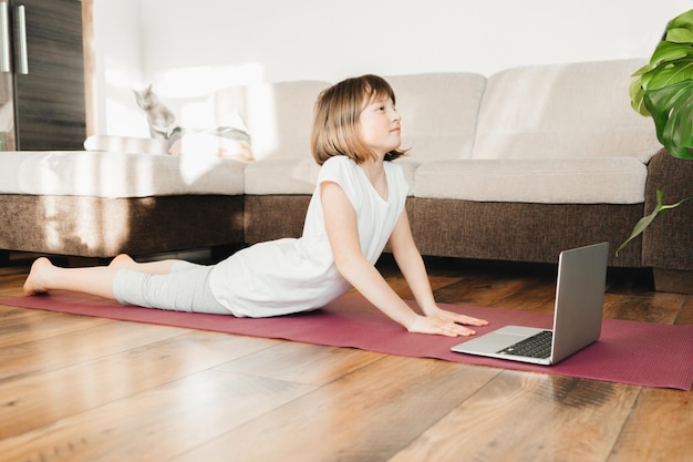 Une jolie fille fait du sport à la maison un enfant apprend le yoga à la maison des sports pour enfants en ligne