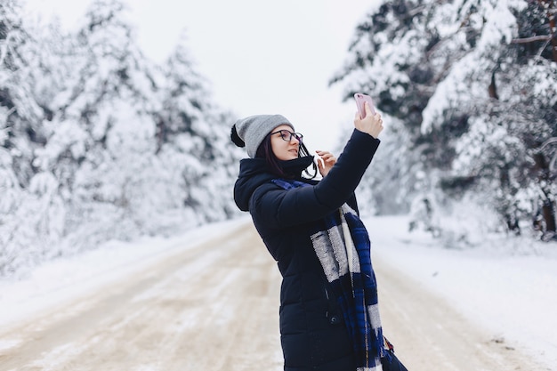 Une jolie fille fait un selfie au milieu d&#39;une route forestière enneigée