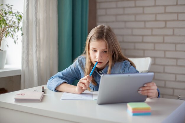 Une jolie fille fait ses devoirs à l'aide d'une tablette