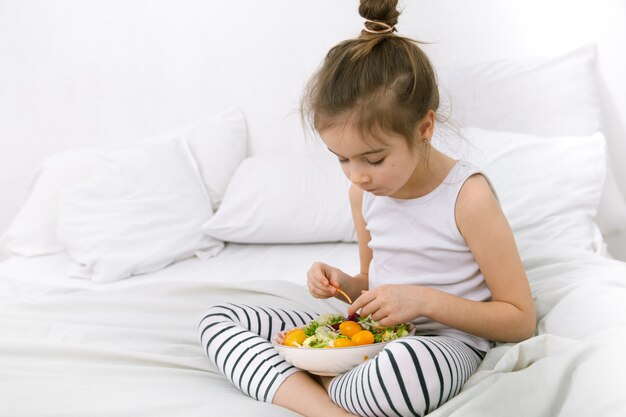 Photo jolie fille avec des fruits et légumes sur le lit blanc