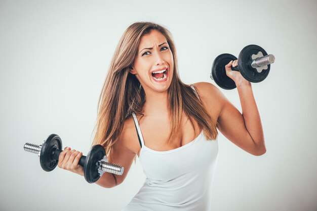 Jolie fille frustrée se poussant tout en soulevant des poids.