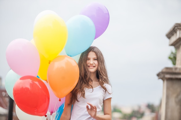 Jolie fille avec de gros ballons en latex colorés posant dans la rue d'une vieille ville