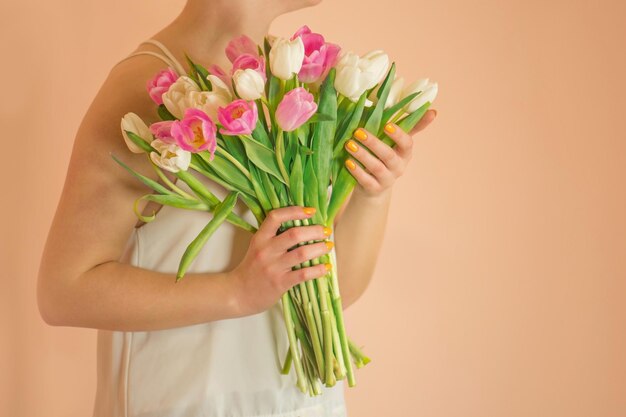 Jolie fille heureuse avec bouquet de fleurs sur fond beige Jeune charmante fille souriante tenant un gros bouquet de tulipes sur fond beige clair