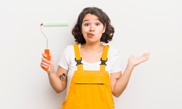 Jolie fille hispanique se sentant perplexe et confuse et doutant du concept de maison de peinture