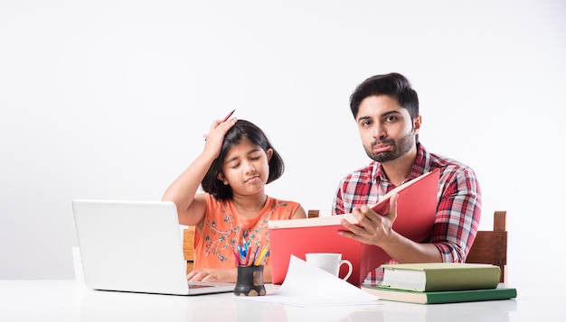 Jolie fille indienne avec son père étudiant ou faisant ses devoirs à la maison à l'aide d'un ordinateur portable et de livres - concept d'enseignement en ligne