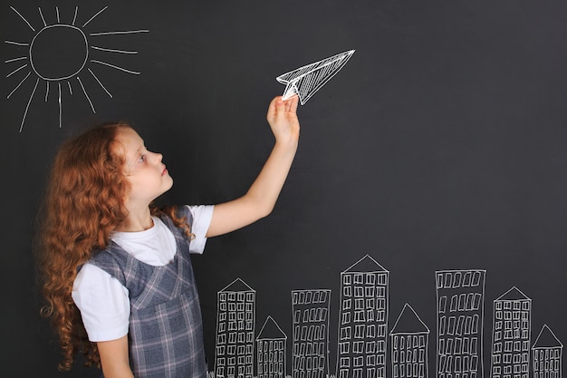 Jolie fille jetant un avion en papier, dessin sur tableau noir