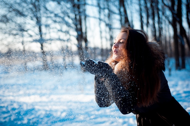 Jolie fille jette de la neige dans un parc d'hiver