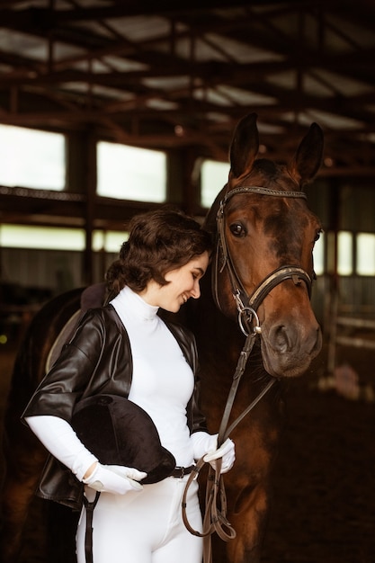 Jolie fille jockey à côté d'un beau cheval brun tirant en gros plan belle jeune fille se tient à côté de ...