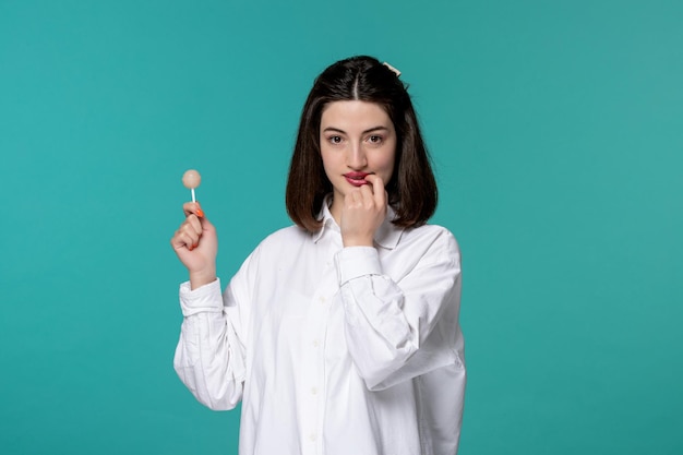 Jolie fille jolie brune jeune fille douce en chemise blanche se mordant le doigt avec un bonbon