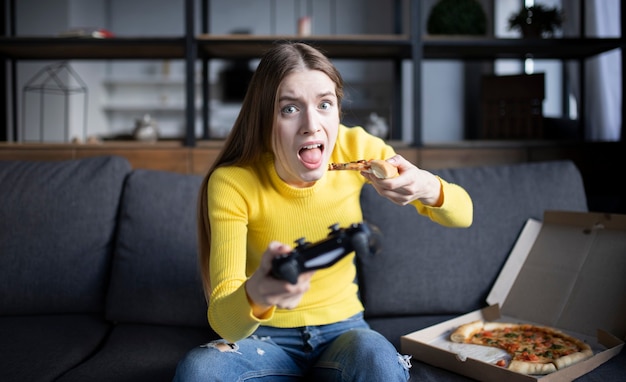 Jolie fille joue au jeu sur la console et mange de la pizza