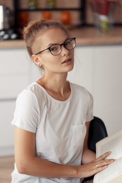 Jolie fille lit un livre à la table de la cuisine à la maison