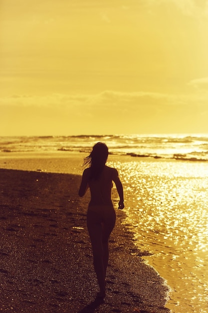 Jolie fille en maillot de bain jaune s'exécutant sur la plage de sable