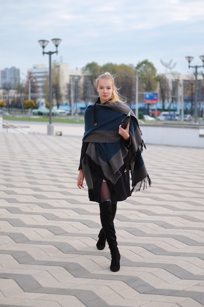 Jolie fille en manteau de laine chaud et écharpe enroulée autour du cou marchant dans la rue. Hipster de style urbain.