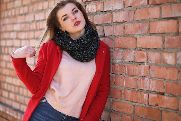 Jolie fille en manteau rouge sur fond de mur de briques