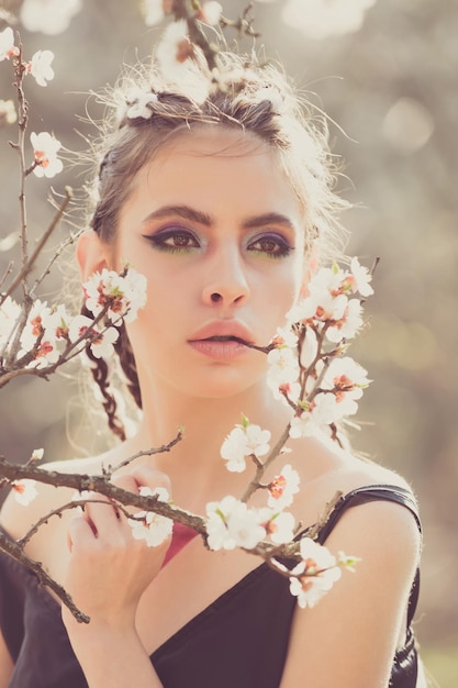 Jolie fille avec un maquillage à la mode parmi les fleurs de cerisier en fleurs au printemps