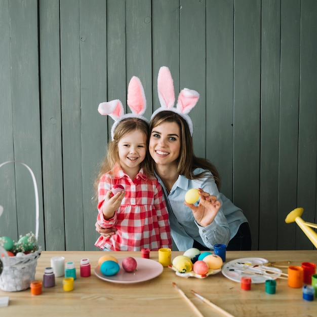 Jolie fille et mère en oreilles de lapin debout avec des oeufs colorés