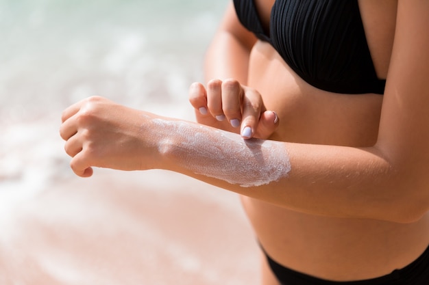 Jolie fille met de la crème solaire sur sa main à la plage.