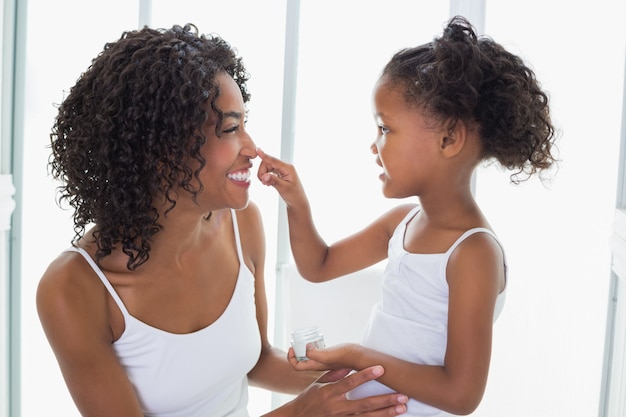 Jolie fille mettant la crème pour le visage sur le nez de la mère