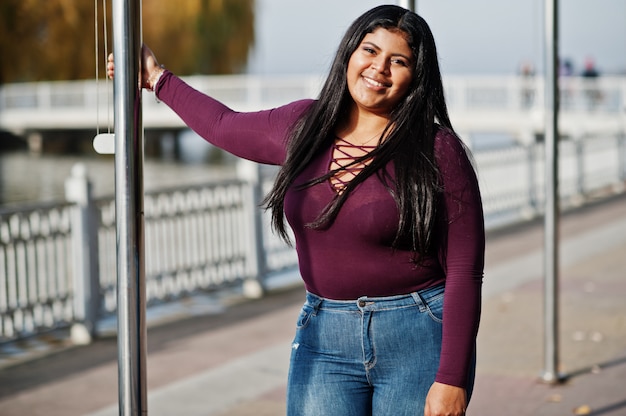 Jolie fille modèle latino xxl d'Equateur porte un chemisier violet posé contre le lac.