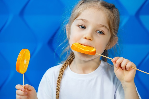 Jolie fille avec des oranges, elle les mange sur fond bleu