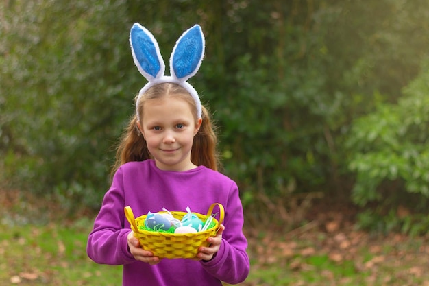 Jolie fille avec des oreilles de lapin et panier d'œufs colorés sur fond naturel costume de lapin de Pâques amusant enfance