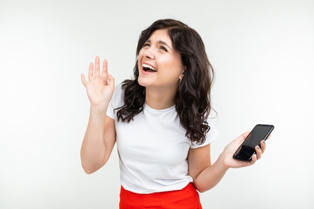 Jolie fille parlant sur le haut-parleur d'un téléphone sur un fond de studio blanc