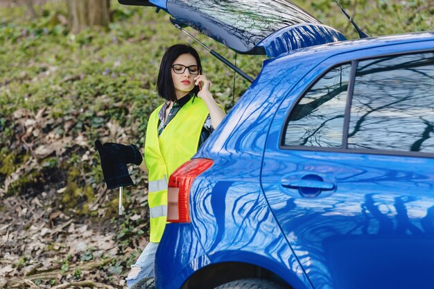 Photo jolie fille parlant par téléphone près de la voiture sur la route en veste de sécurité