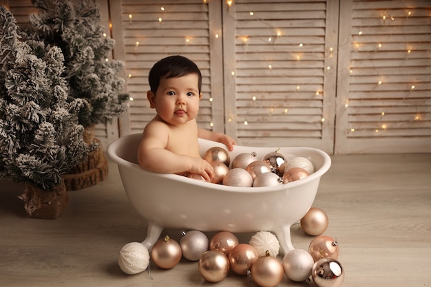 Une jolie fille à la peau foncée est assise dans un bain avec des jouets pour arbres de Noël