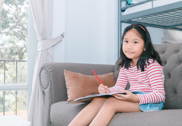 Jolie fille peindre ou faire ses devoirs sur le canapé dans le salon apprendre et se détendre