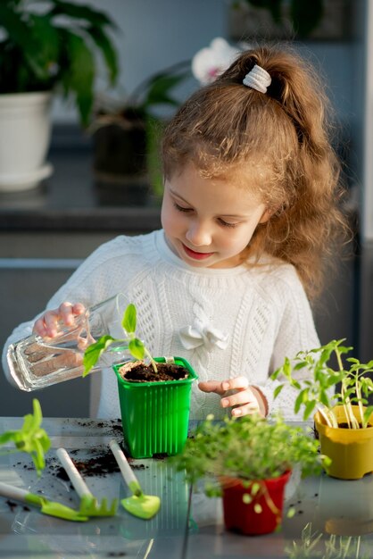 Une jolie fille plante à la maison dans des pots écologiques Elle porte un pull blanc Le jardin de la maison Passe-temps