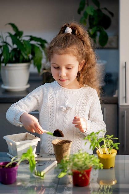 Une jolie fille plante à la maison dans des pots écologiques Elle porte un pull blanc Le jardin de la maison Passe-temps