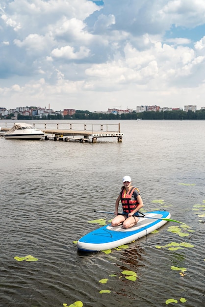 Jolie fille porter un gilet de sauvetage se repose et prend un bain de soleil sur une planche de surf après l'entraînement d'un mode de vie estival actif